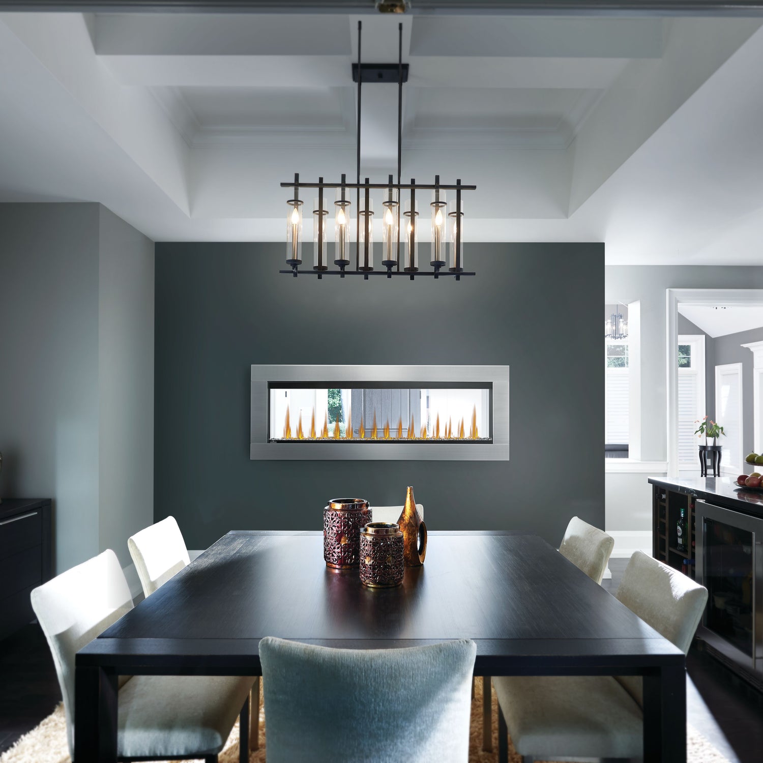 Modern dining room with a black table and chairs, featuring a chandelier and wall-mounted fireplace.